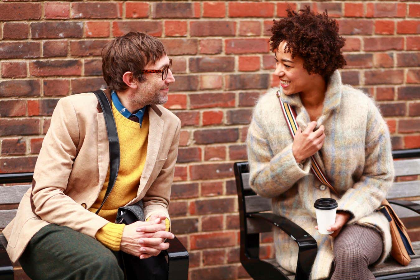 Young african american woman and caucasian men sitting on benches in the London city and having fun discussion. Commuters on break.